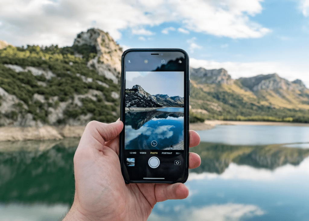 person taking a picture of mountain landscape with their phone for instagram or social media